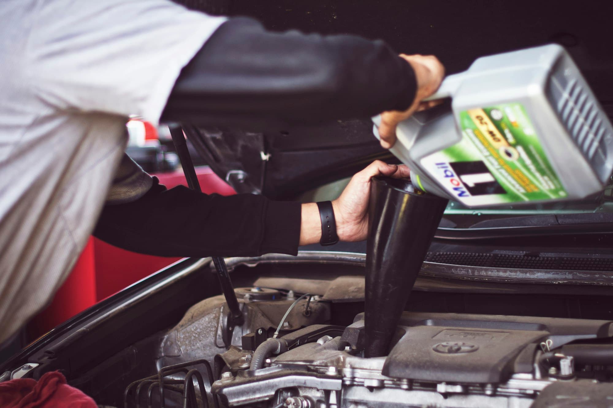A mechanic adding motor oil to an engine bay during a service.