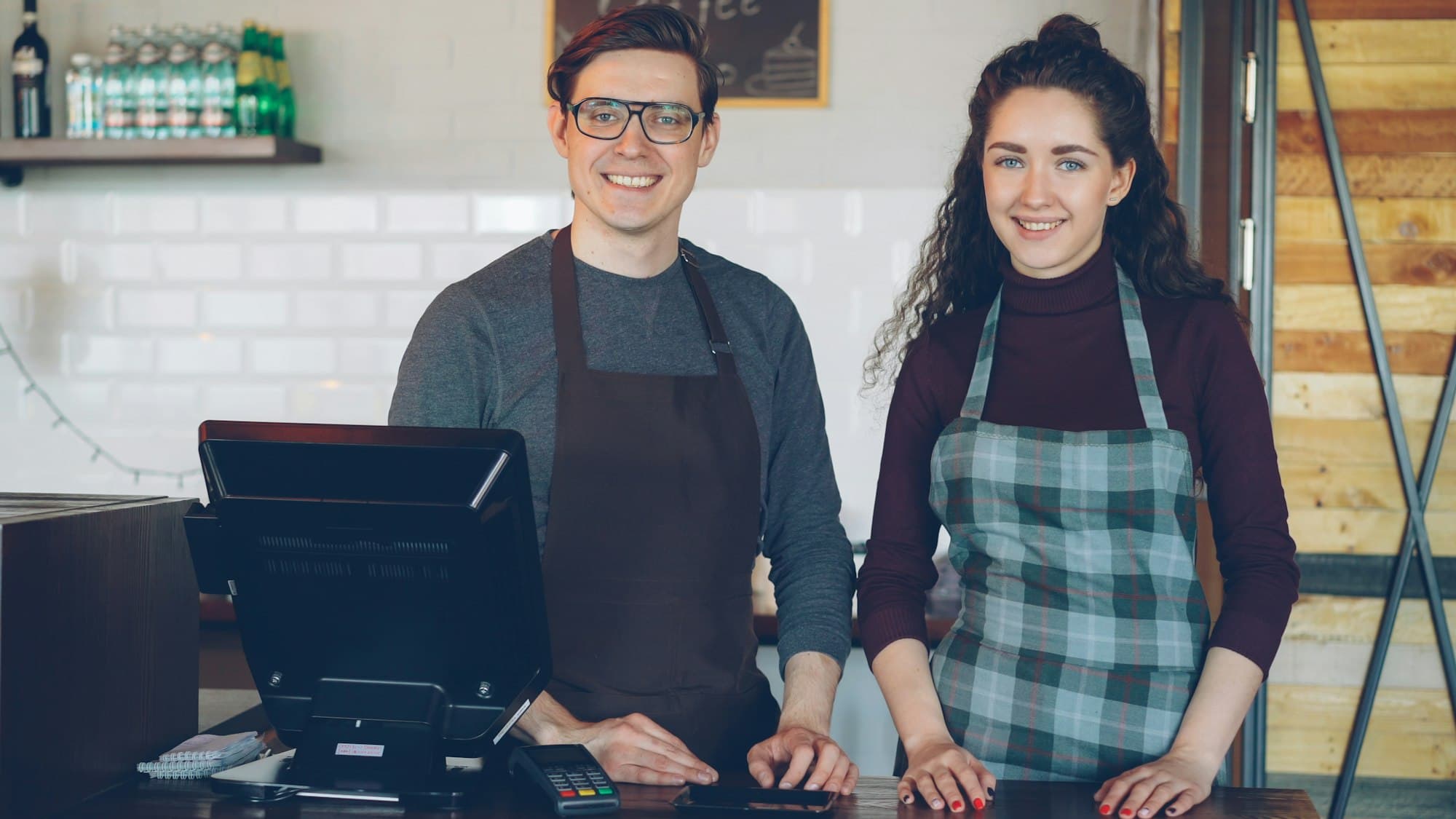 Two cafe owners standing behind their POS counter ready for service.