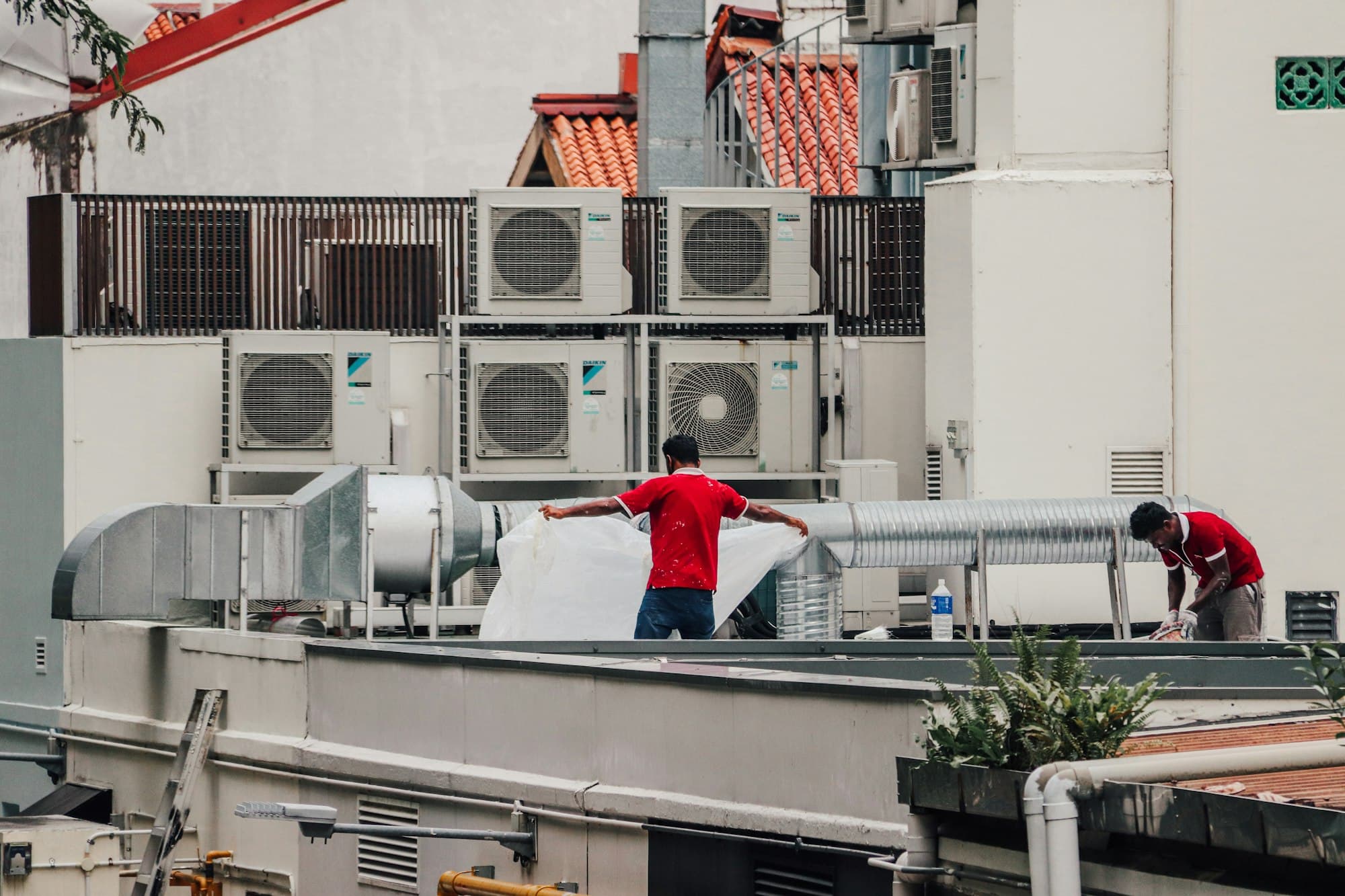 Two HVAC technicians servicing rooftop air-conditioning condensers.